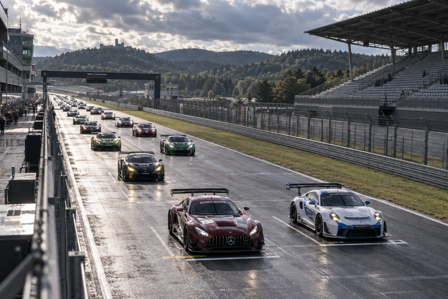 A packed endurance racing grid on a German circuit beneath grandstands and a dramatic cloudy sky.